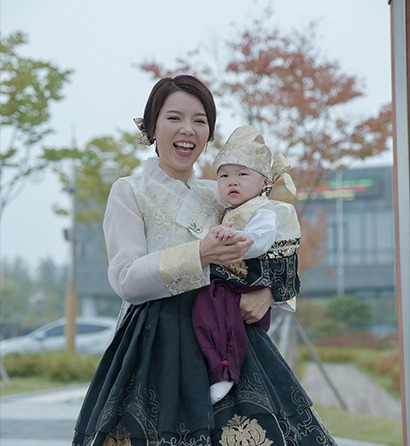 야외에서 엄마 품에 안긴 지훈이 — 엄마 활짝 웃는 자연광 컷